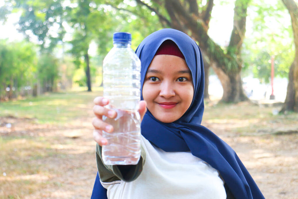 Uma mulher hijab bebe água mineral
 - Foto, Imagem