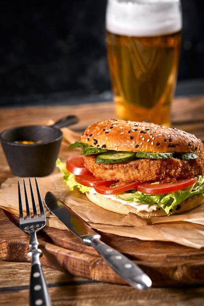 Juicy burger, french fries, sauces and a glass of cold beer on a dark wooden background. copy space, fast food set, food photo - Фото, изображение