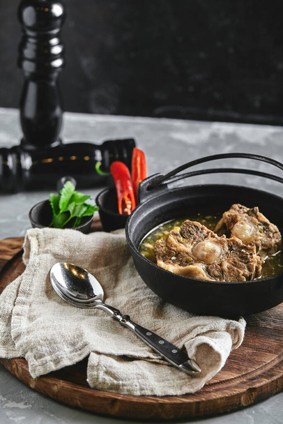 Shurpa soep in een gietijzeren pot op tafel op een grijze achtergrond. Traditionele oosterse keuken. - Foto, afbeelding