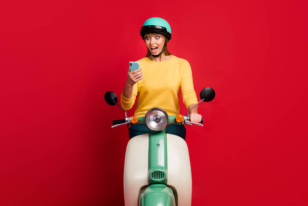 Portrait of her she nice attractive lovely addicted amazed cheerful cheery girl sitting on moped using cell browsing comment feedback isolated on bright vivid shine vibrant red color background - 写真・画像