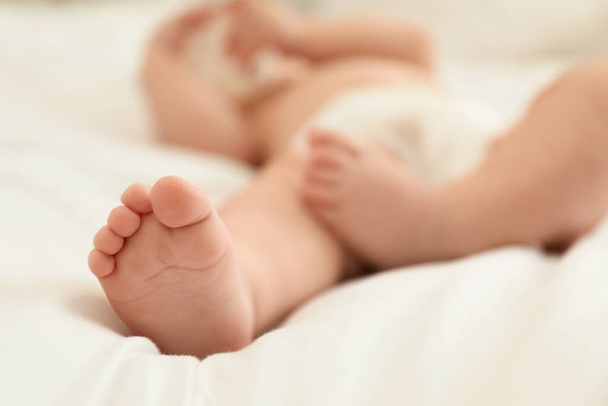 Cute little baby in diaper on bed, closeup - Foto, afbeelding