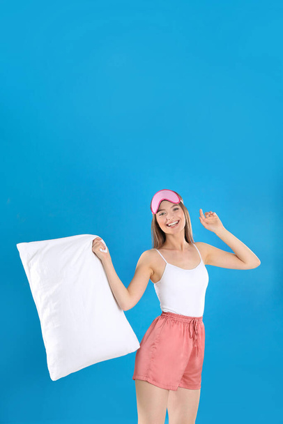 Junge Frau mit Kopfkissen und Schlafmaske auf blauem Hintergrund - Foto, Bild