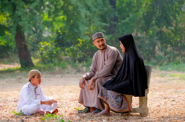 父と母と息子を持つイスラム教徒の家族は森の近くに滞在し、昼光と一緒に話をする. - 写真・画像