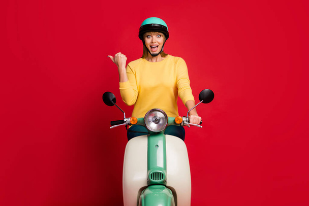 Look. Full length photo of funny courier lady driving speed deliver service worker direct finger empty space wear yellow sweater teal helmet isolated red color background - Φωτογραφία, εικόνα