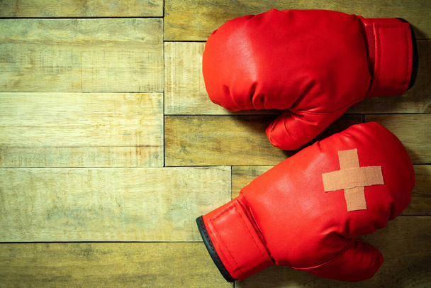 Red boxing gloves placed on wooden floor at the gym. Adhesive plaster across each other on boxing gloves. Idea of getting hurt or combat losing business rivals. Concept of fighting giving up boxing. - Photo, Image