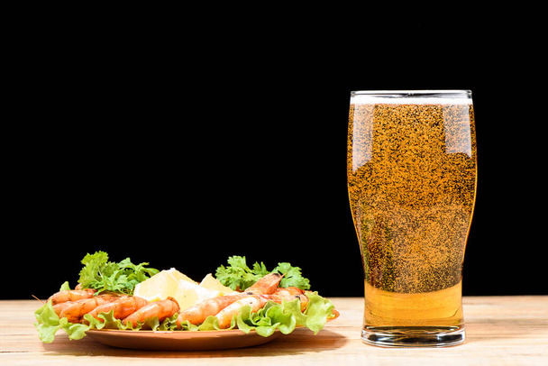 Freshly poured beer on a wooden table. Plate with shrimp, lettuce and slices of lemon. Lager beer. - Photo, image