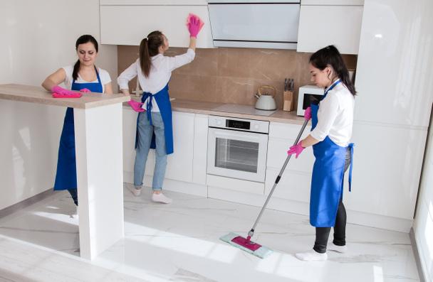 Επαγγελματικός καθαρισμός σπιτιού. Τρία όμορφα κορίτσια καθαρίζουν την κουζίνα.. - Φωτογραφία, εικόνα