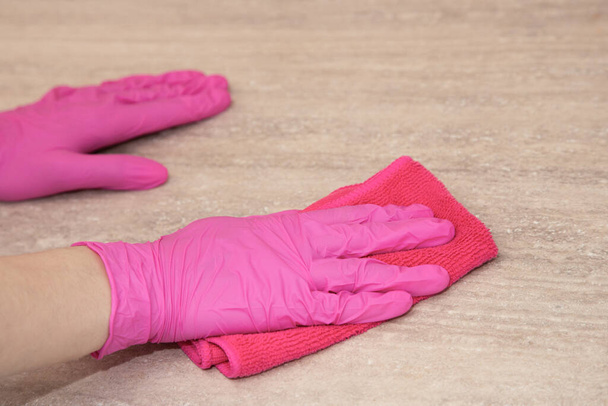 A girl in pink rubber gloves washes a wooden surface with a microfiber cloth. - Zdjęcie, obraz