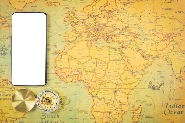 Conceitos de acessórios de viagem: É hora de viajar ao redor do mundo - A imagem de um mapa do mundo com acessórios essenciais - telefone inteligente e bússola. Estilo de tom vintage. Imagem vista superior
. - Foto, Imagem