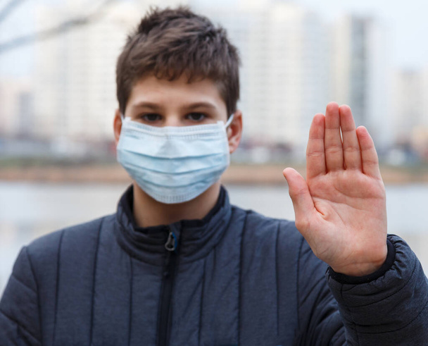 Young cute caucasian boy wearing protective mask against the corona virus on the street. Teenager in surgical face mask to prevent from virus Covid 19 in the city. Close up portrait - Photo, Image