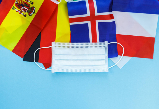 Medizinische Maske mit Flaggen von Spanien, Frankreich, Deutschland auf blauem Hintergrund. Maske zum Schutz vor Staub, Umweltverschmutzung, Viren. - Foto, Bild