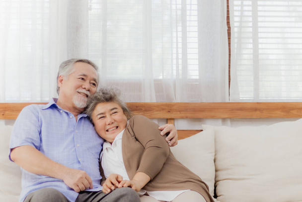 Mutlu Asyalı son sınıf çifti romantik bir anda evdeki kanepede birlikte kalıyorlar. Emekli, yaşlı, gülümseyen, büyük anne ve büyük baba aşığının kucaklaşması, sevgiyle kucaklaşması ve el ele tutuşması. Yaşlıların emeklilik hayatı - Fotoğraf, Görsel