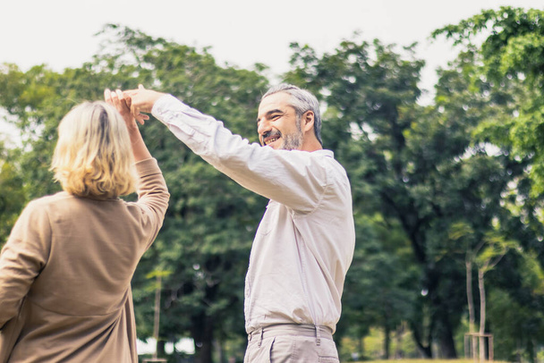 Kedves idős, mosolygós pár férfi és nő táncolnak a parkban egy romantikus pillanatban. Meleg szívű házasság, szerető kötődés és kapcsolat. Férj és feleség szerelmesek. Boldog nyugdíjasok fényképe - Fotó, kép