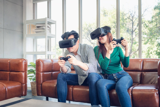 Casal jovem se divertindo enquanto joga jogo de realidade virtual juntos em sua casa. Amor de casal tendo prazer com jogos eletrônicos de óculos VR no sofá. Entretenimento Inovação / Estilo de Vida Conceito
 - Foto, Imagem