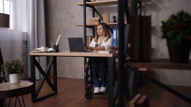 Γυναίκα σε αναπηρική καρέκλα που εκτείνεται κατά τη διάρκεια της εργασίας στο σπίτι - Πλάνα, βίντεο