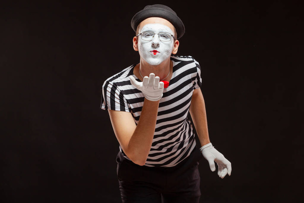 Portrait of male mime artist performing, isolated on black background. Man leaned over to blow a kiss - Foto, Bild