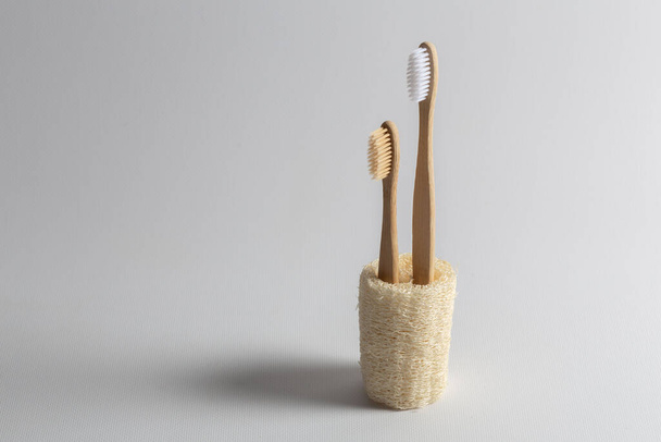 Two toothbrushes made of natural wood, one small for a child, inserted into a natural ecological loofah. On white background. - Photo, Image