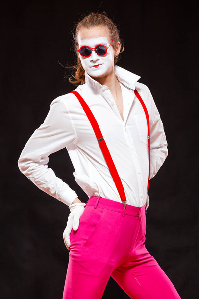 Portrait of male mime artist, isolated on black background. Man in suspenders and pink trousers is posing pointing with hands on his hips - Foto, Bild