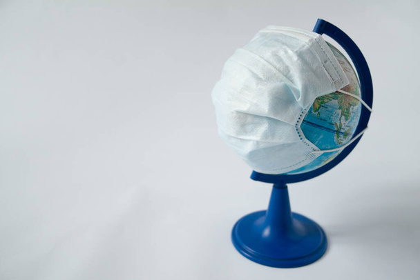Das Konzept einer globalen Pandemie und eine Größenordnung des Coronavirus. Globus in medizinischer Maske auf grauem Hintergrund mit Kopierraum. Verbreitung von Virusinfektionen und Krankheiten in allen Ländern. - Foto, Bild
