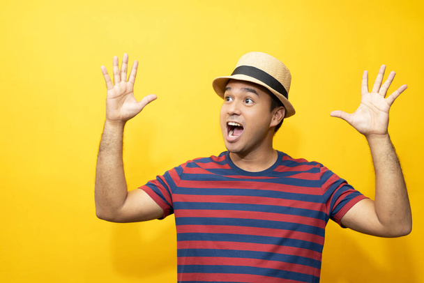 Portrait of cheerful asian man in basic clothing Casual wear red striped T-shirt and wear a hat smiling and show giving thumbs up at camera with showing success. isolated over yellow background. - Foto, Imagem