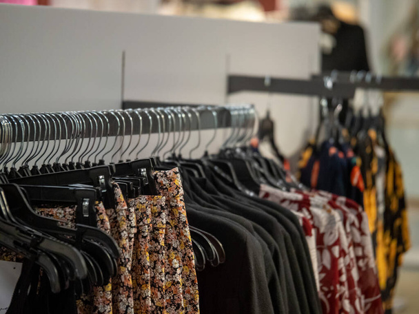 Eine Reihe blumig gemusterter weiblicher Kleidungsstücke auf einem Kleiderständer in einem Designer-Kleiderladen - Foto, Bild
