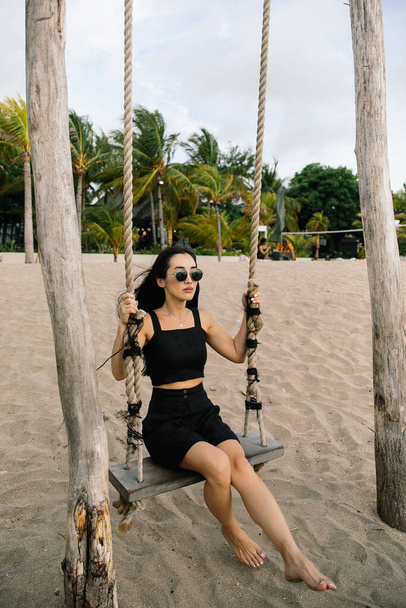 cute little asian girl riding on a swing and having fun on the beach near the ocean on the island of Bali in Indonesia - Fotó, kép