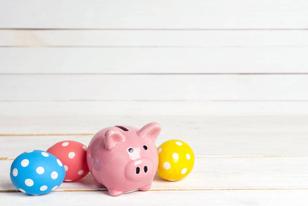 Piggy bank with eggs on a white wooden background. Saving money for easter holidays. Copy space for text. - Foto, Bild