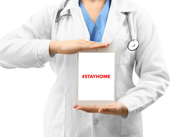 Female doctor with hashtag #STAYHOME on screen of tablet computer on white background. Concept of epidemic - Fotoğraf, Görsel