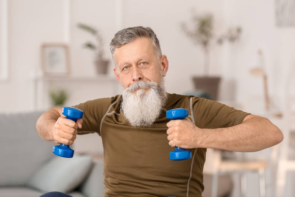 Sportif yaşlı adam evde dambıllarla antrenman yapıyor. - Fotoğraf, Görsel