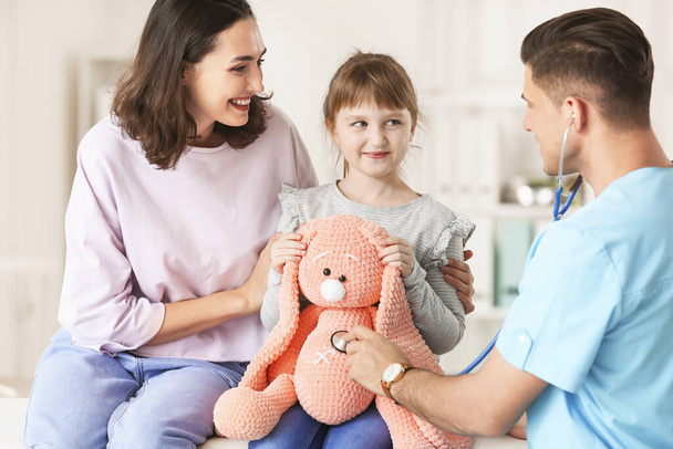 Pediatra com brinquedo mostrando a menina como usar estetoscópio na clínica
 - Foto, Imagem