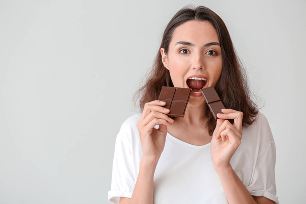Schöne junge Frau isst leckere Schokolade auf weißem Hintergrund - Foto, Bild