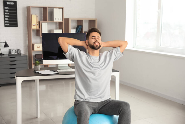 Homem fazendo exercícios com bola de fitness no escritório
 - Foto, Imagem