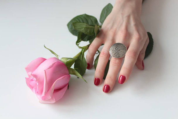 A high angle shot of a female hand with a beautiful silver ring on a rose with green leaves - Zdjęcie, obraz