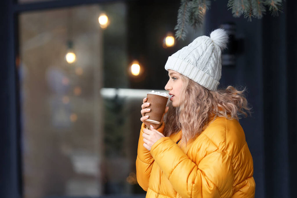 Beautiful young woman drinking hot cocoa outdoors - Фото, изображение