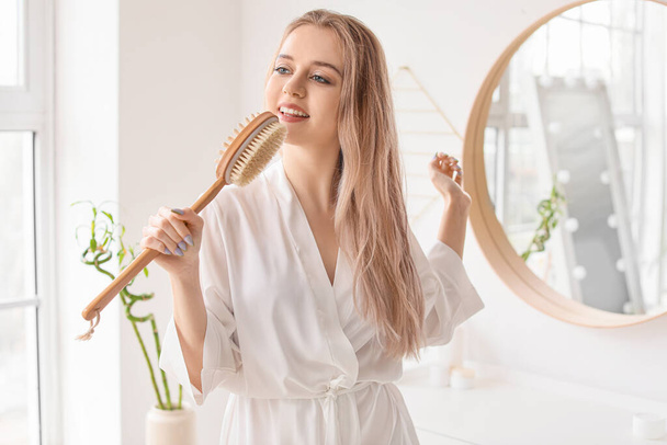 Beautiful young woman with brush in bathroom - Fotografie, Obrázek