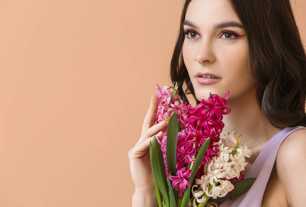 Mooie jonge vrouw met hyacint bloemen op kleur achtergrond - Foto, afbeelding