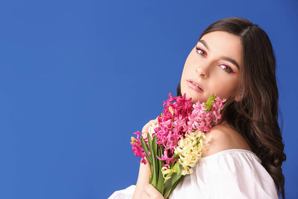 Όμορφη νεαρή γυναίκα με λουλούδια υάκινθος στο φόντο χρώμα - Φωτογραφία, εικόνα