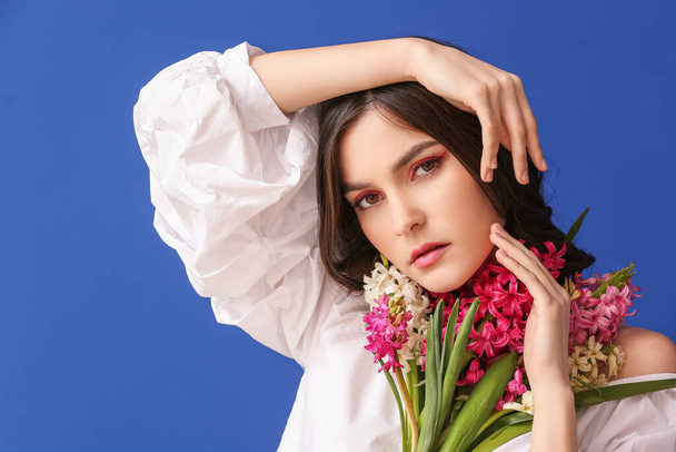 Schöne junge Frau mit Hyazinthenblüten auf farbigem Hintergrund - Foto, Bild