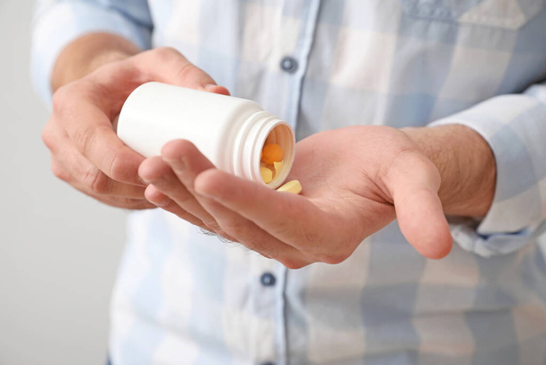 Jongeman met pillen op lichte achtergrond, close-up - Foto, afbeelding