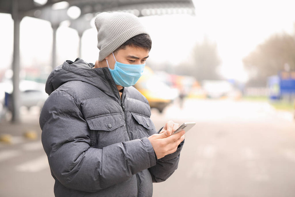 Asian man in protective mask and with mobile phone on city street. Concept of epidemic - Photo, Image