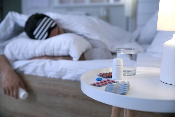 Tabletták álmatlanság az asztalon a hálószobában a fiatalember - Fotó, kép