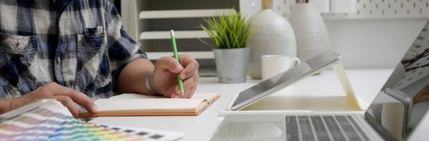 Sivunäkymä mies graafinen suunnittelija työskentelee luonnos paperi, tabletti ja kannettava toimisto työpöytä suunnittelija tarvikkeet
 - Valokuva, kuva