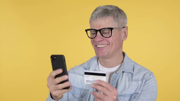 オンラインショッピングカジュアル老人によるスマートフォン、黄色の背景 - 写真・画像
