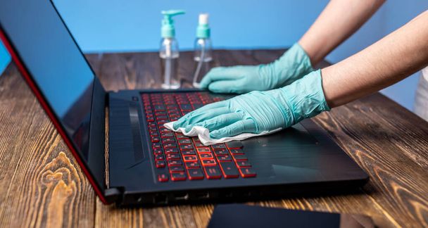 As mãos das mulheres em luvas estéreis manuseiam seu local de trabalho limpando um guardanapo com um laptop desinfetante. Limpeza e higiene na luta contra os vírus
 - Foto, Imagem