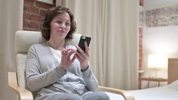 Atractiva anciana usando Smartphone en el dormitorio
 - Foto, Imagen