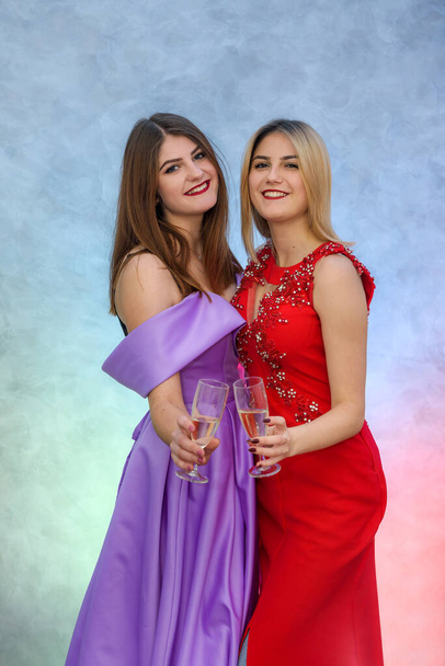 Blondynka i brunetka w eleganckich sukniach wieczorowych pozowanie z kieliszkami szampana - Zdjęcie, obraz