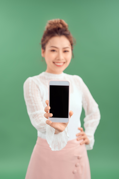 close-up portret van een glimlachende aziatische vrouw tonen blanco scherm mobiele telefoon terwijl staan geïsoleerd over groene achtergrond. - Foto, afbeelding