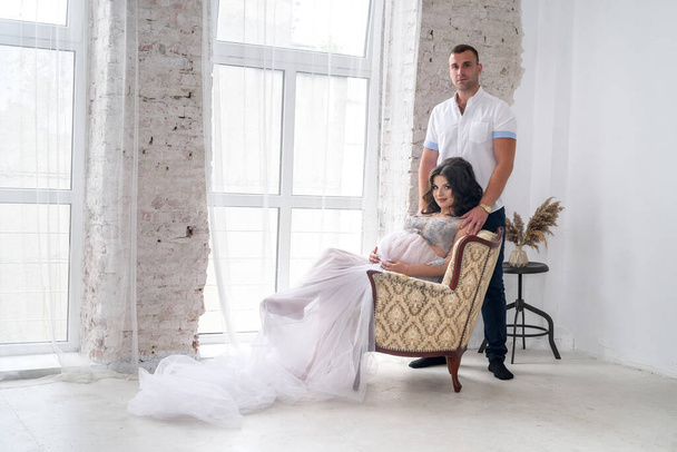 Esperando. Feliz pareja embarazada en ropa de moda posando en el estudio
 - Foto, Imagen