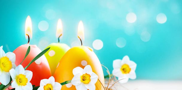 Velikonoční barevné svíčky vejce s narcisy květiny na rozmazaném modrém pozadí s bokeh světla. Rozumím. Měkké zaměření - Fotografie, Obrázek