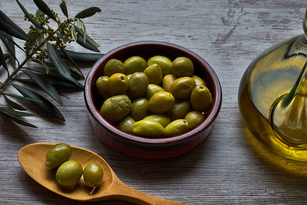 Green olives in bowl and wooden teaspoon - Photo, Image